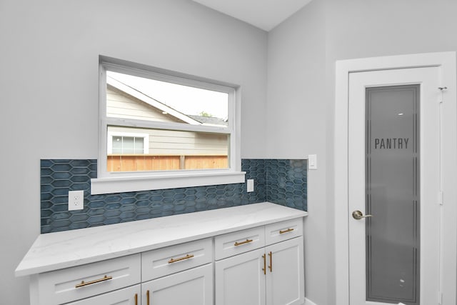 kitchen with white cabinets, light stone countertops, and backsplash