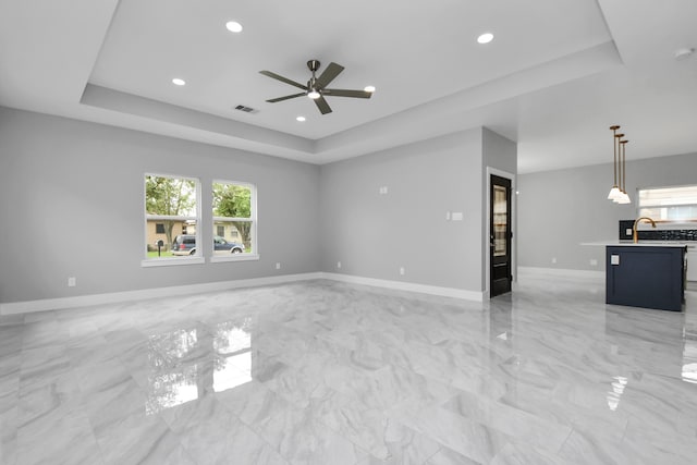 unfurnished living room featuring a tray ceiling, ceiling fan, and sink