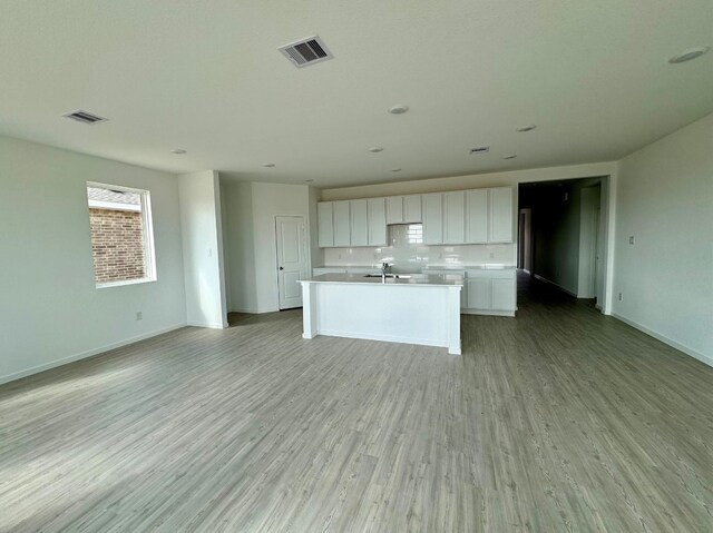 kitchen featuring a center island with sink, white cabinets, decorative backsplash, sink, and light hardwood / wood-style flooring