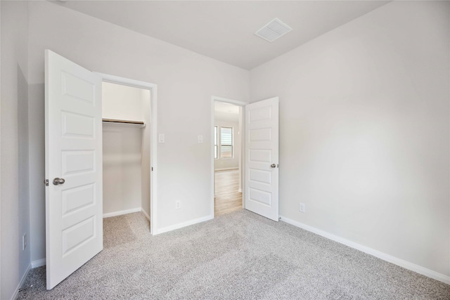 unfurnished bedroom featuring a closet, light colored carpet, and a spacious closet