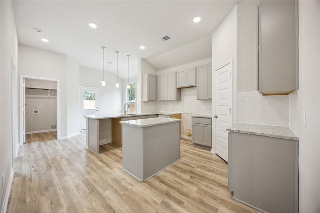 kitchen with gray cabinets, light wood-type flooring, a kitchen island, kitchen peninsula, and hanging light fixtures