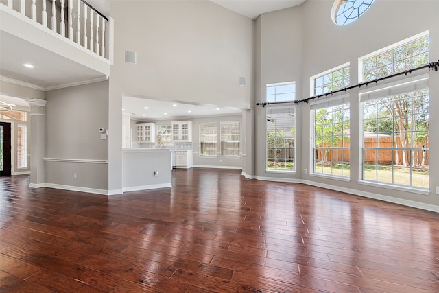 unfurnished living room featuring dark wood-type flooring, plenty of natural light, a towering ceiling, and ornamental molding