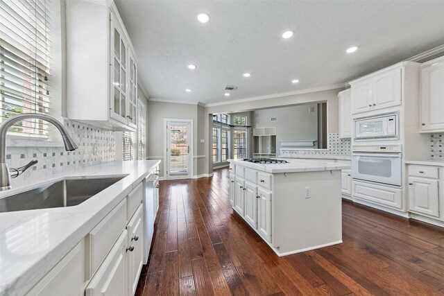 kitchen featuring light stone countertops, white appliances, white cabinets, a kitchen island, and sink