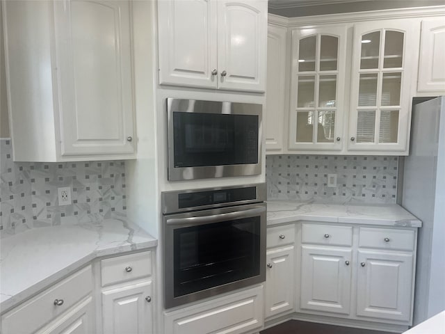 kitchen with decorative backsplash, light stone counters, white cabinetry, and appliances with stainless steel finishes