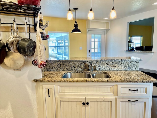 kitchen featuring light stone counters, sink, hanging light fixtures, and a healthy amount of sunlight