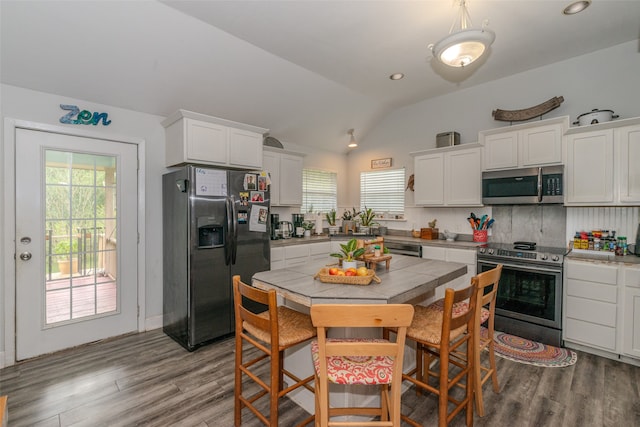 kitchen with appliances with stainless steel finishes, vaulted ceiling, a wealth of natural light, and hardwood / wood-style flooring