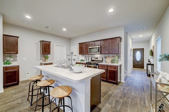 kitchen with a kitchen breakfast bar, a kitchen island with sink, stainless steel appliances, decorative backsplash, and light wood-type flooring