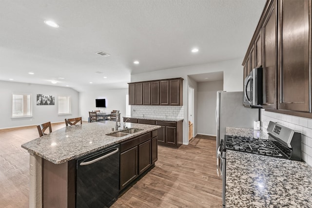 kitchen featuring a kitchen island with sink, stainless steel appliances, sink, light stone countertops, and decorative backsplash