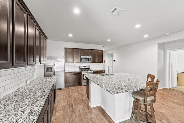 kitchen featuring light hardwood / wood-style flooring, a kitchen bar, light stone counters, an island with sink, and appliances with stainless steel finishes