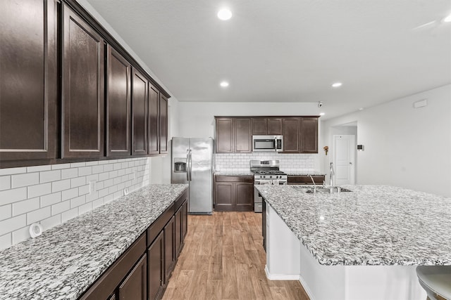 kitchen featuring backsplash, stainless steel appliances, sink, light stone counters, and light wood-type flooring