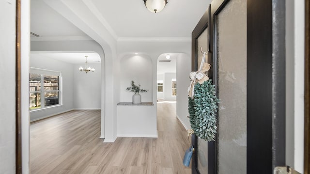 corridor featuring light wood-type flooring, an inviting chandelier, and crown molding