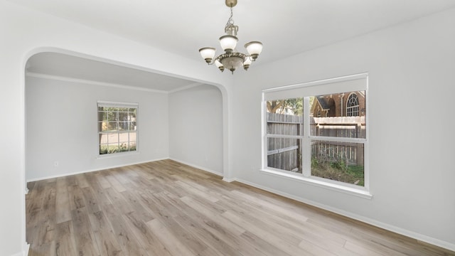 spare room featuring light wood-type flooring, an inviting chandelier, plenty of natural light, and crown molding