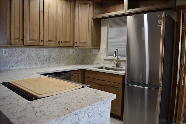 kitchen with light stone counters, backsplash, stainless steel fridge, and sink