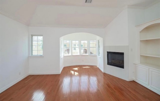 unfurnished living room featuring crown molding, lofted ceiling, hardwood / wood-style flooring, and built in shelves