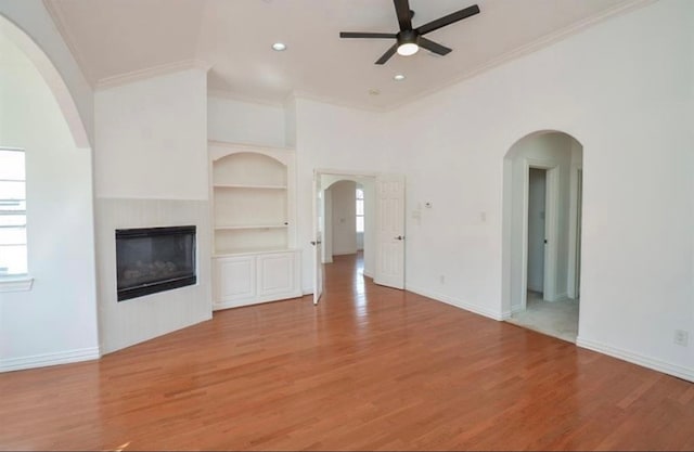 unfurnished living room featuring built in shelves, ceiling fan, light hardwood / wood-style floors, and crown molding