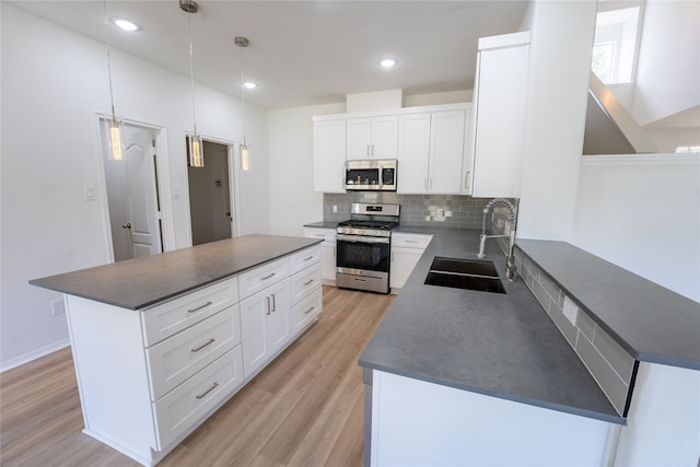 kitchen with white cabinets, decorative light fixtures, light wood-type flooring, stainless steel appliances, and sink