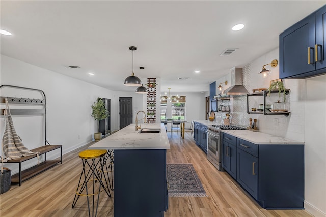 kitchen featuring blue cabinetry, sink, stainless steel stove, wall chimney exhaust hood, and light hardwood / wood-style floors