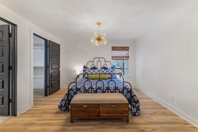 bedroom with a walk in closet, light hardwood / wood-style floors, a notable chandelier, and a closet