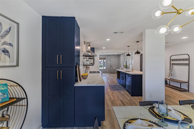 kitchen with a chandelier, sink, hanging light fixtures, blue cabinets, and light hardwood / wood-style floors