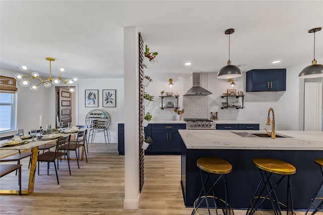 kitchen with blue cabinetry, wall chimney exhaust hood, sink, and pendant lighting