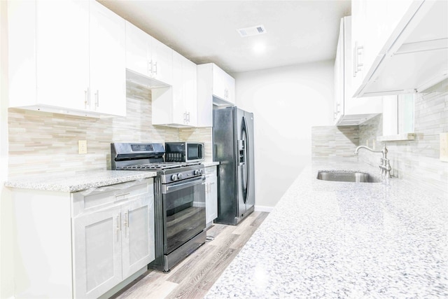 kitchen featuring light stone countertops, stainless steel appliances, sink, light wood-type flooring, and white cabinets