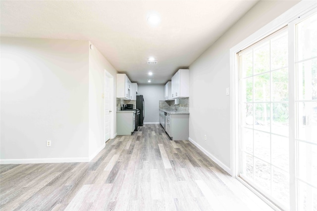 kitchen with black fridge, backsplash, white cabinetry, and light hardwood / wood-style flooring