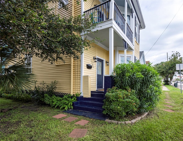 view of exterior entry featuring a balcony and a yard