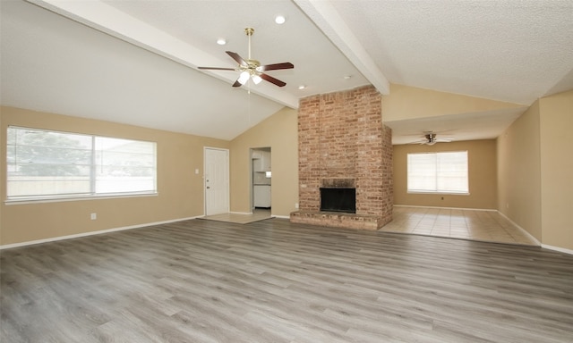 unfurnished living room featuring light hardwood / wood-style flooring, a brick fireplace, beamed ceiling, ceiling fan, and a textured ceiling