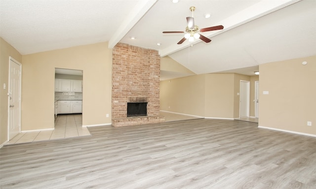 unfurnished living room featuring beamed ceiling, a textured ceiling, light hardwood / wood-style flooring, a brick fireplace, and ceiling fan