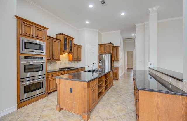 kitchen with an island with sink, appliances with stainless steel finishes, decorative columns, crown molding, and sink