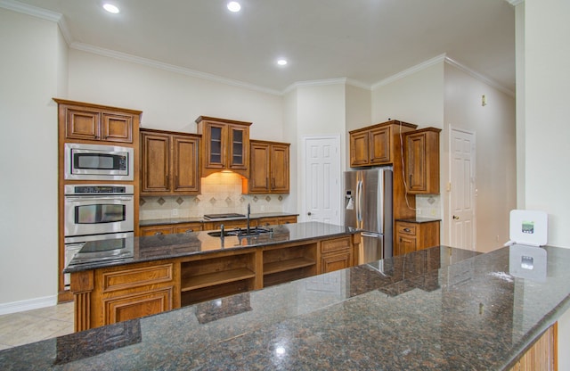 kitchen with dark stone countertops, stainless steel appliances, ornamental molding, and an island with sink