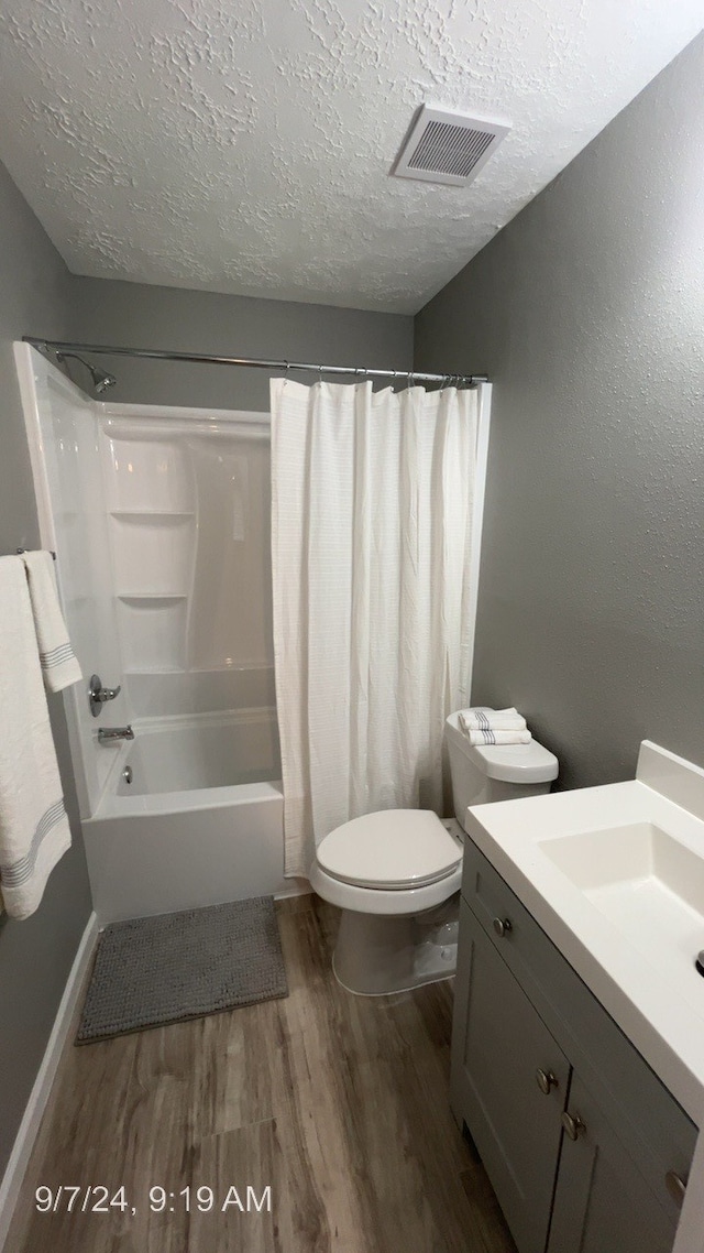 full bathroom featuring hardwood / wood-style floors, toilet, shower / tub combo with curtain, vanity, and a textured ceiling