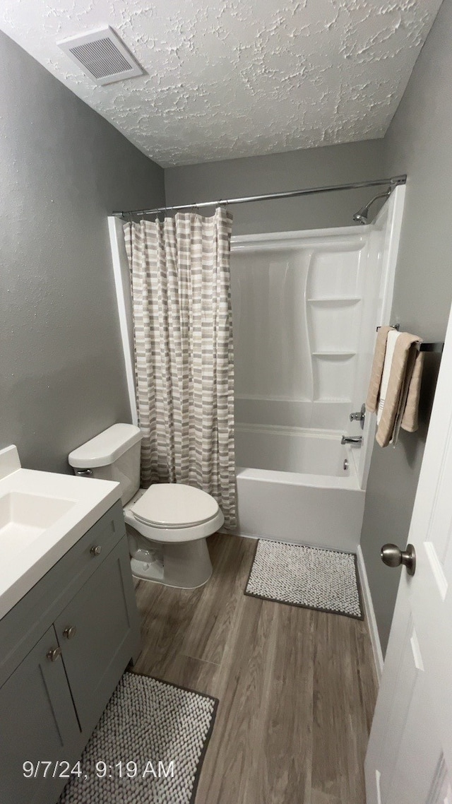 full bathroom with toilet, wood-type flooring, shower / tub combo, vanity, and a textured ceiling