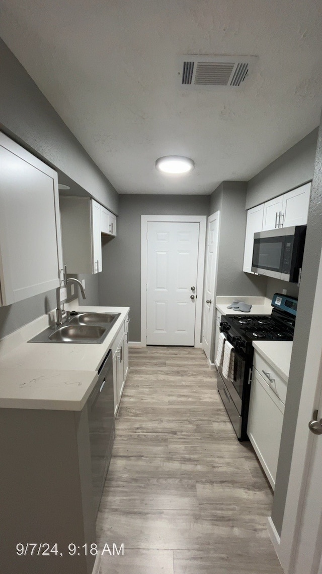 kitchen with stainless steel appliances, sink, light wood-type flooring, and white cabinets