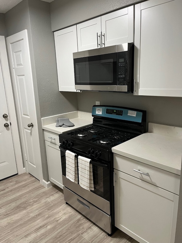 kitchen featuring appliances with stainless steel finishes, white cabinetry, light stone counters, and light hardwood / wood-style floors