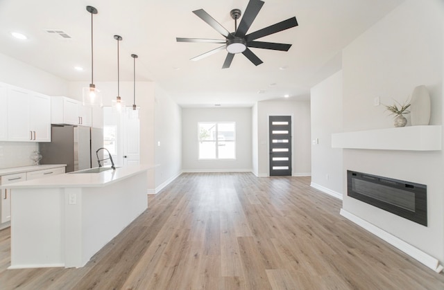 kitchen with white cabinets, a kitchen island with sink, hanging light fixtures, and light hardwood / wood-style floors