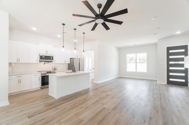 kitchen with light wood-type flooring, a kitchen island with sink, white cabinetry, hanging light fixtures, and stainless steel appliances