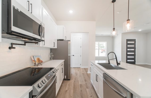 kitchen with appliances with stainless steel finishes, hanging light fixtures, white cabinetry, and sink