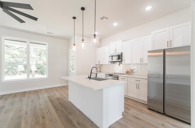 kitchen featuring appliances with stainless steel finishes, decorative light fixtures, light wood-type flooring, and white cabinets