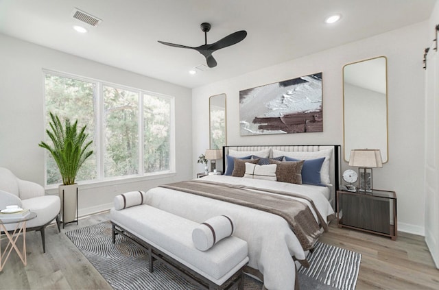 bedroom with light hardwood / wood-style flooring, ceiling fan, and a barn door