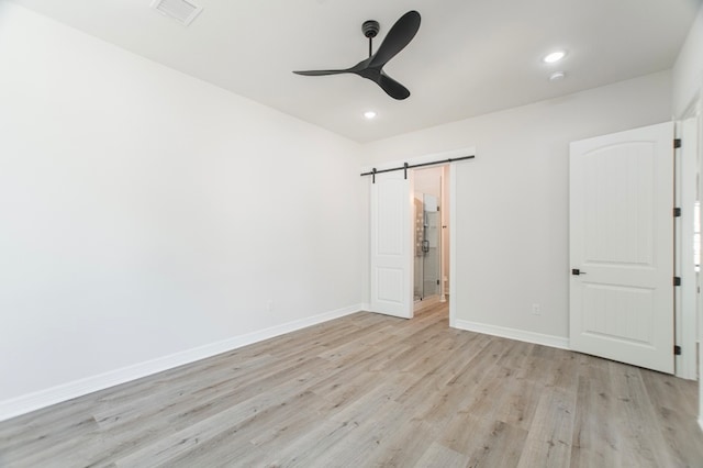 unfurnished bedroom with a barn door, light wood-type flooring, and ceiling fan