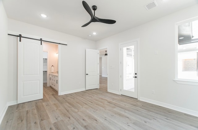 unfurnished bedroom featuring ceiling fan, light wood-type flooring, ensuite bath, and a barn door