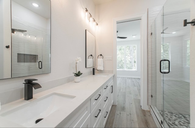 bathroom with hardwood / wood-style floors, baseboard heating, a shower with door, and vanity