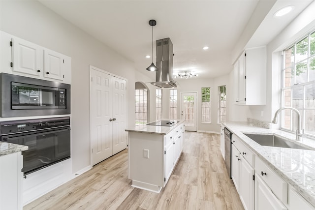 kitchen with light stone counters, white cabinetry, sink, black appliances, and island exhaust hood