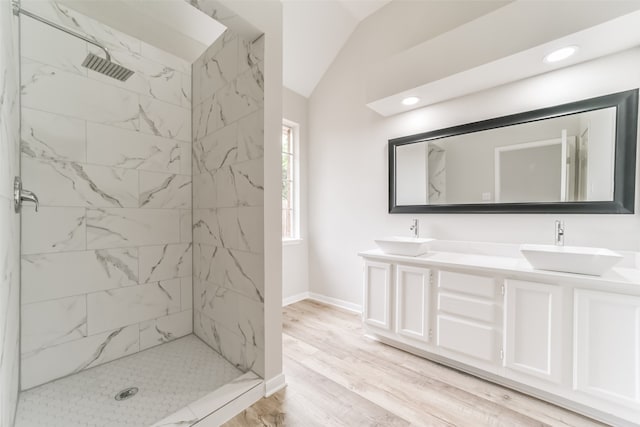 bathroom with lofted ceiling, wood-type flooring, a tile shower, and vanity