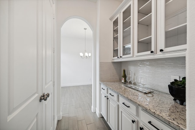 bar featuring decorative light fixtures, hardwood / wood-style floors, light stone countertops, white cabinetry, and decorative backsplash