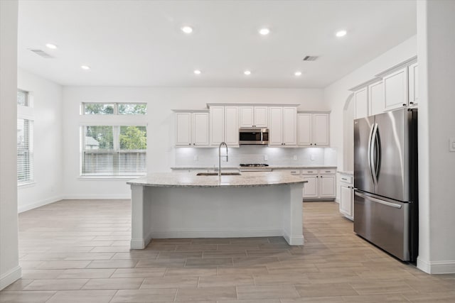 kitchen with appliances with stainless steel finishes, a kitchen island with sink, sink, light wood-type flooring, and white cabinets