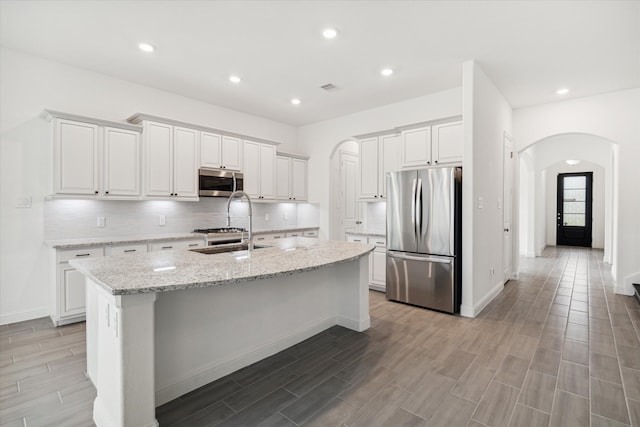 kitchen with appliances with stainless steel finishes, light stone countertops, a center island with sink, and white cabinetry