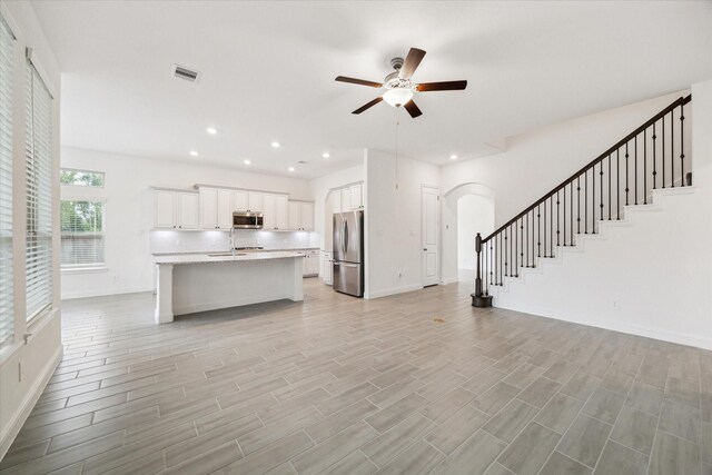 kitchen with a kitchen island with sink, light wood-type flooring, white cabinetry, stainless steel appliances, and ceiling fan