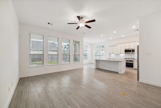 unfurnished living room featuring light wood-type flooring, ceiling fan, and sink